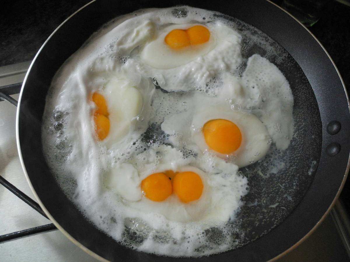 Stainless steel poaching pan for eggs with four individual cups on stovetop